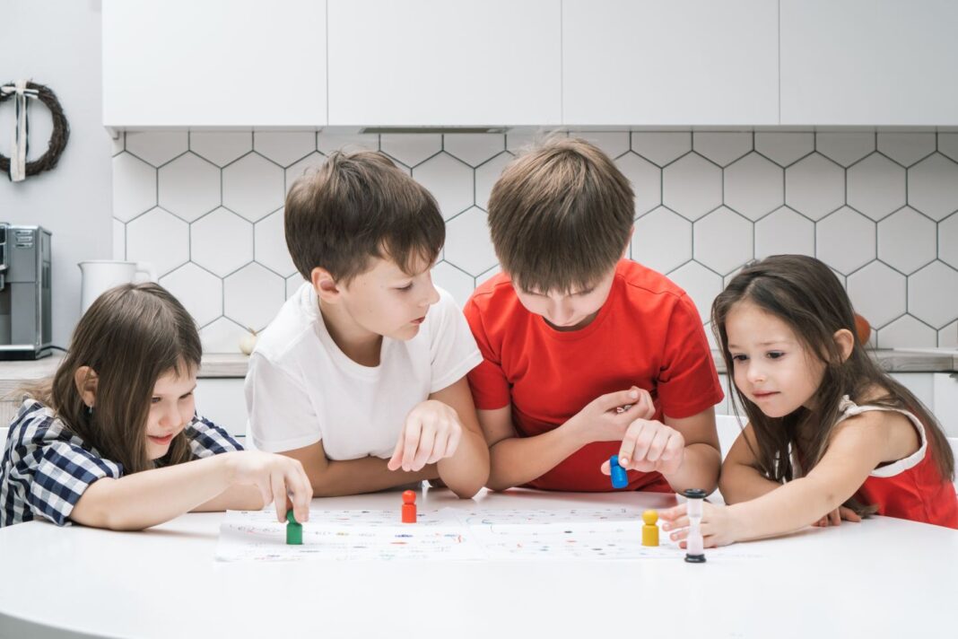 Four blissful, smiling kids playing board games and choosing colorful figures on table in kitchen. Children development gry dla dzieci