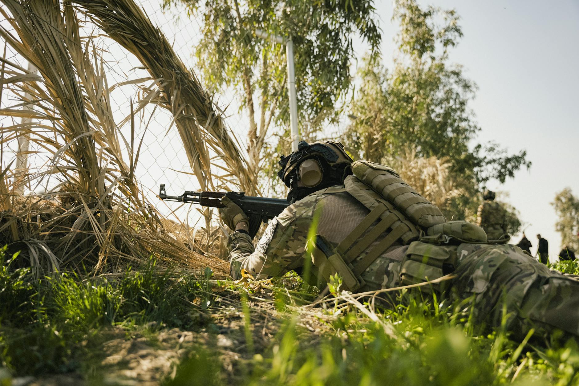 Żołnierz w taktycznym oporządzeniu celuje z karabinu w leśnym terenie